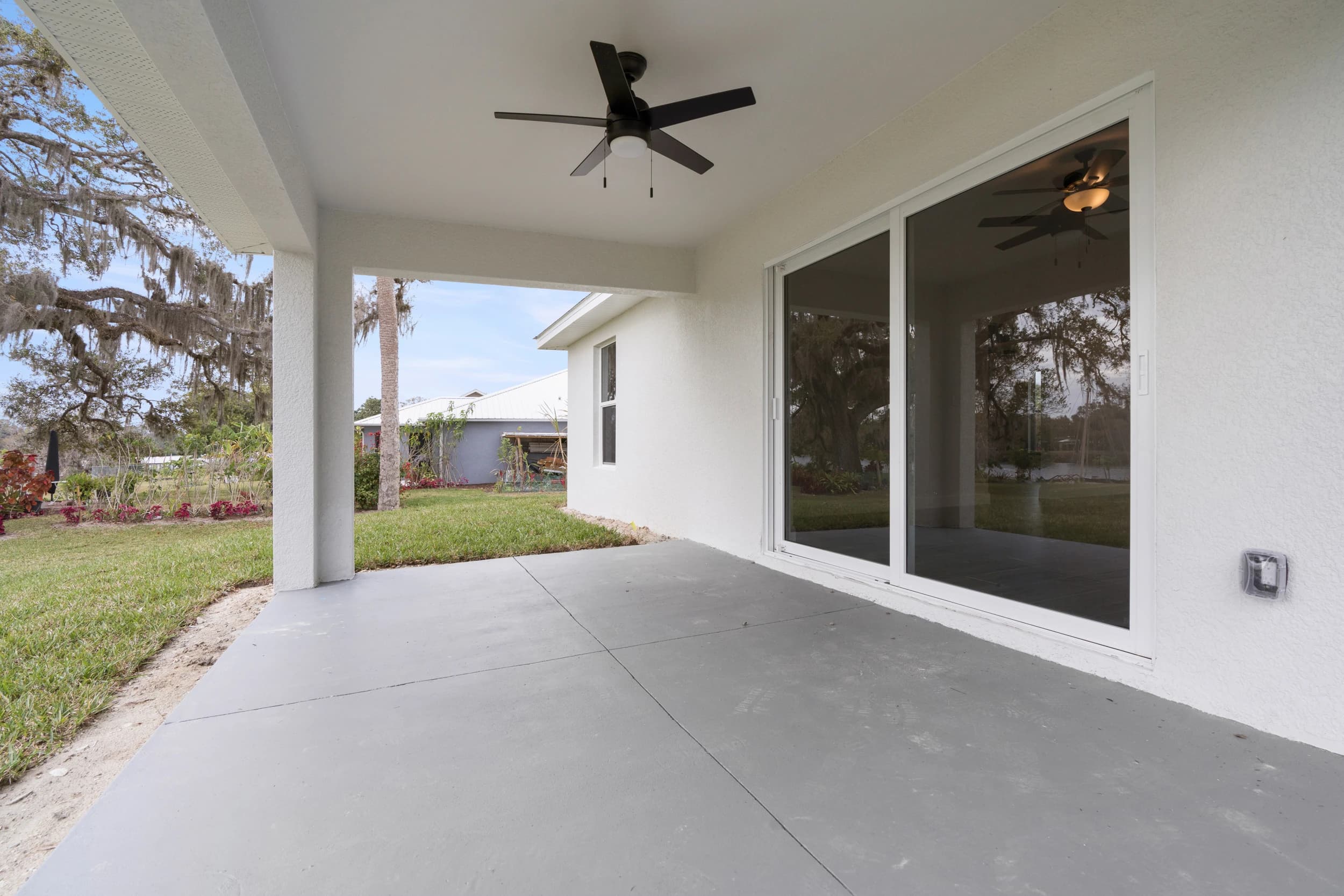Beautiful covered patio in a newly built home in Florida by Vreeland Roofing. This outdoor living space features a ceiling fan and sliding glass doors leading to the interior, perfect for relaxation and entertainment.