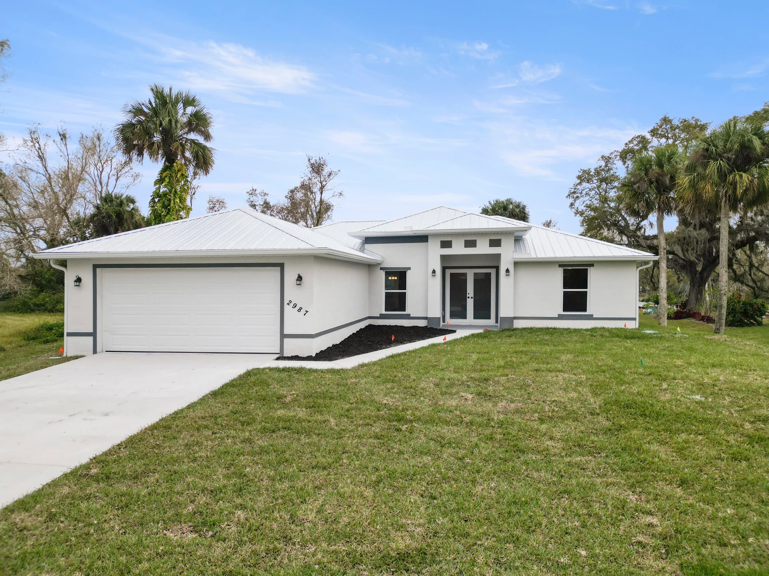 Newly constructed modern custom home in Florida by Vreeland Roofing. Featuring a sleek white exterior, energy-efficient windows, a two-car garage, and a metal roof for durability. Surrounded by lush landscaping and a spacious front yard, this home exemplifies expert craftsmanship and high-quality construction.