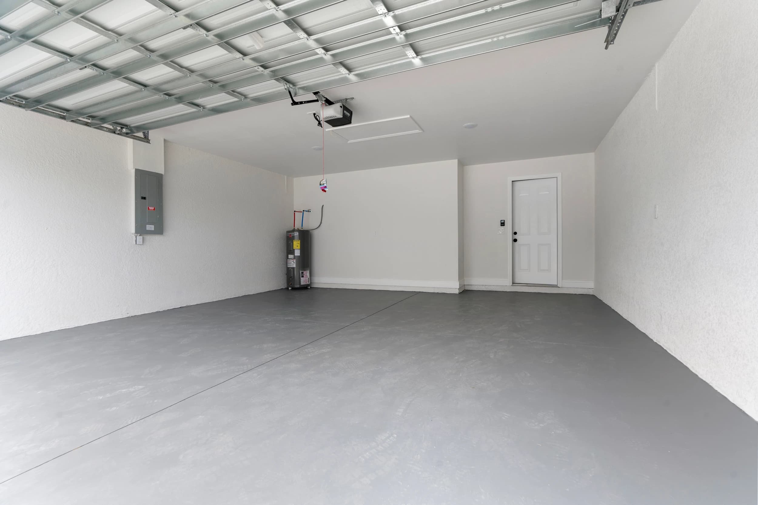 Spacious two-car garage in a newly built custom home by Vreeland Roofing in Florida. Features a durable epoxy-coated floor, a smart garage door opener, bright LED lighting, and an efficient water heater. Designed for functionality, storage, and convenience in modern home construction.